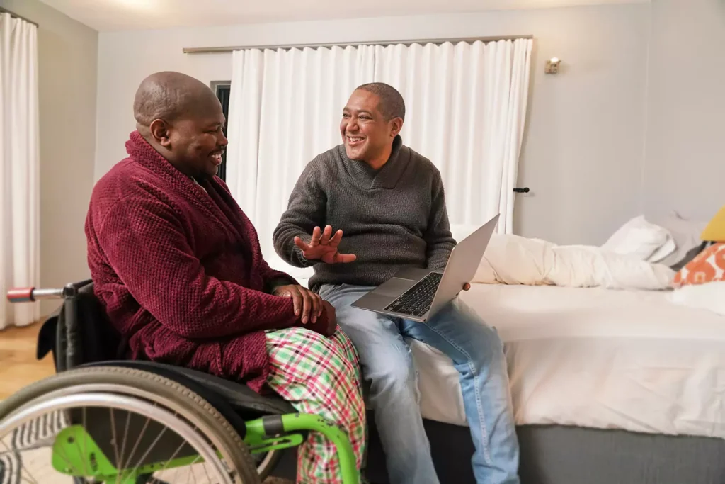 A physically disabled man and his brother are laughing together while indoors