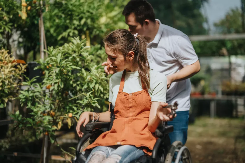 Two friends, both with disabilities are fruit picking together in a garden